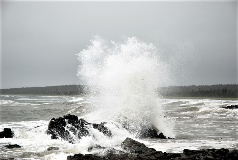 A wave crashes on the rocks in front of the ocean.